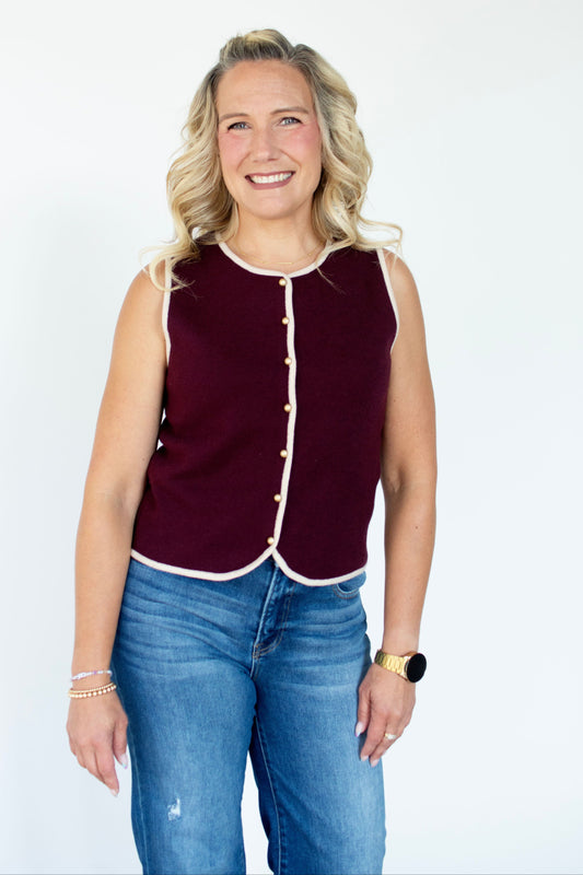 Woman wearing a maroon sleeveless top with white trim and blue jeans on a white background