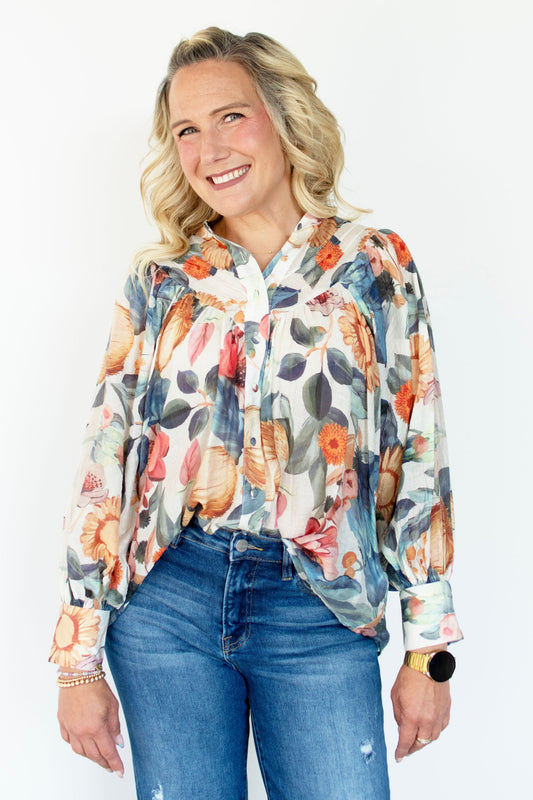 Woman wearing a colorful floral blouse and blue jeans against a white background