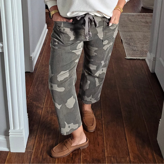 A woman stands in a hallway wearing a white crewneck sweatshirt with 'OHIO' printed in red across the chest, paired with gray and white camouflage drawstring pants and tan slip-on shoes